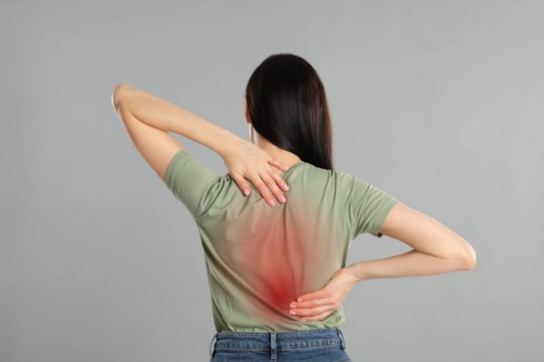 Woman suffering from pain in back on light grey background